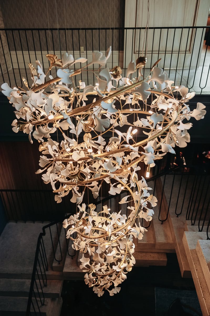 Overhead view of a cascading gold and porcelain floral chandelier above a stone staircase at The Switch House by Cescaphe, Philadelphia, PA.