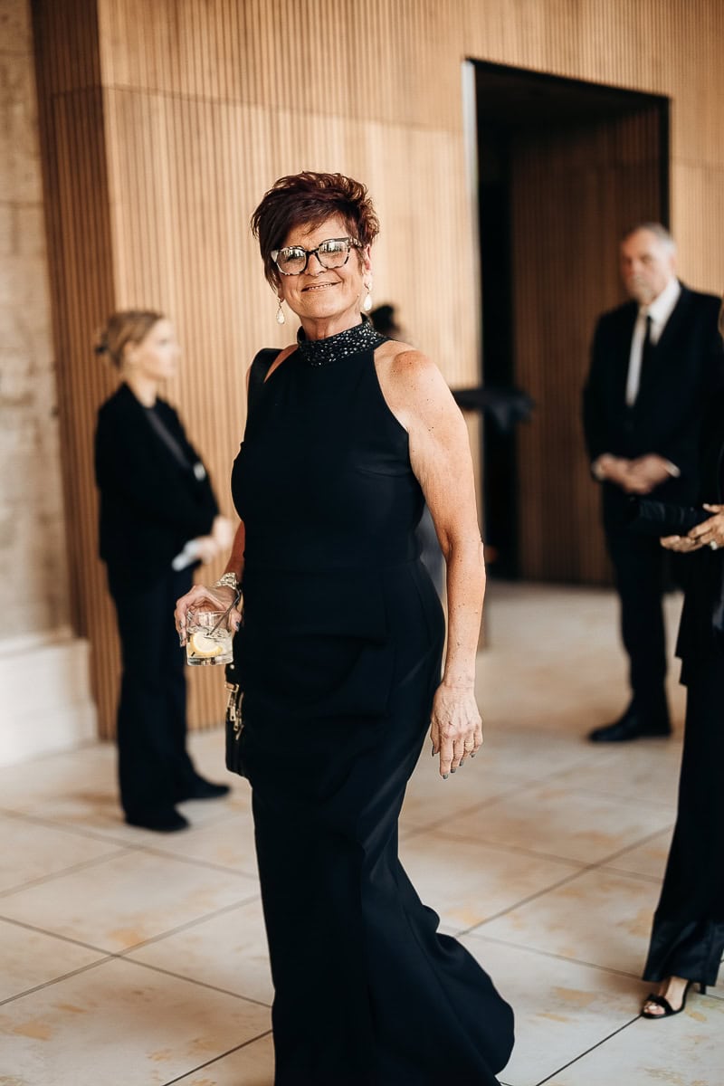Guest in black beaded‑neck gown holding a lemon cocktail in a modern, wood‑lined lobby with blurred guests, at The Switch House, Philadelphia.
