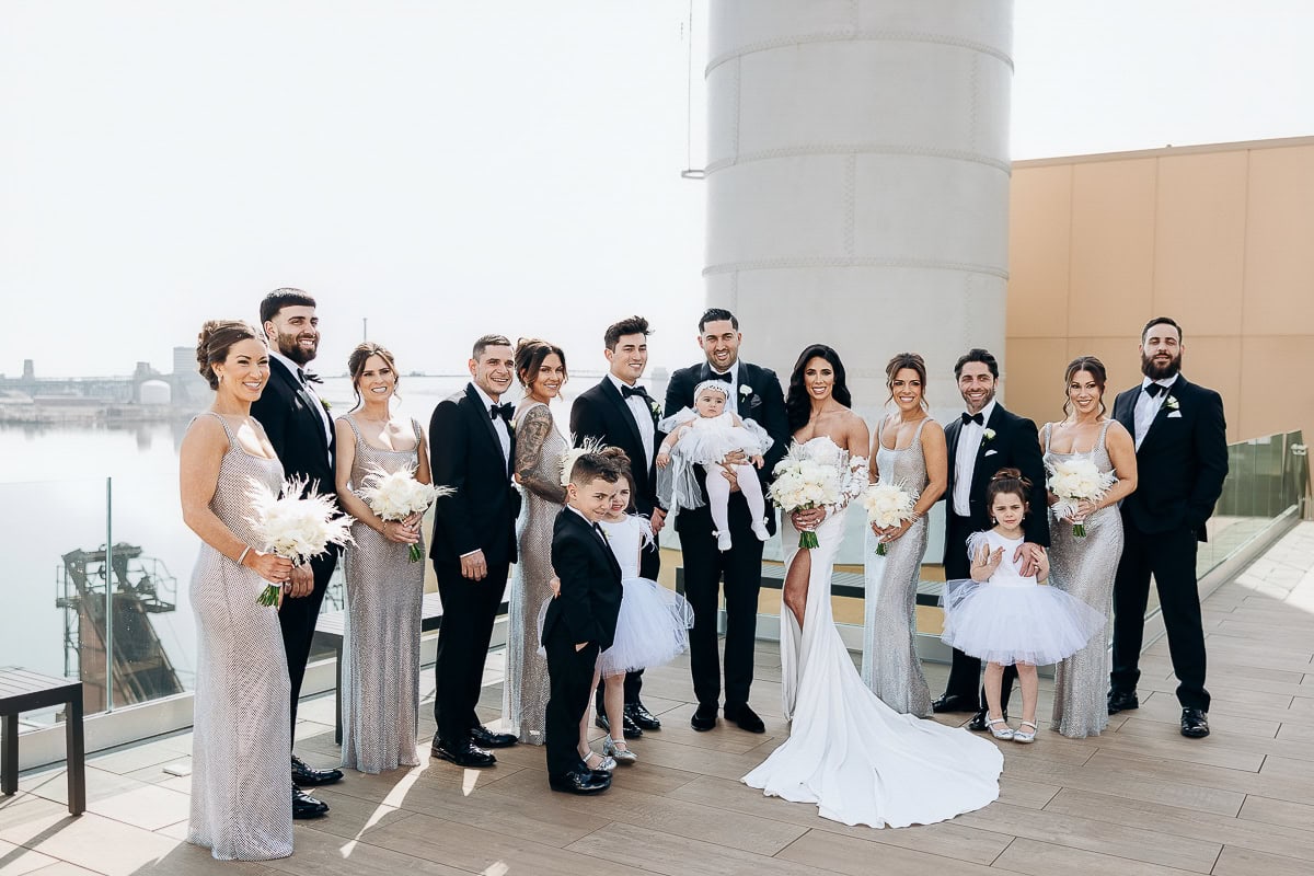 Bridal party in silver gowns and black tuxedos on a riverfront rooftop at The Switch House by Cescaphe, Philadelphia.