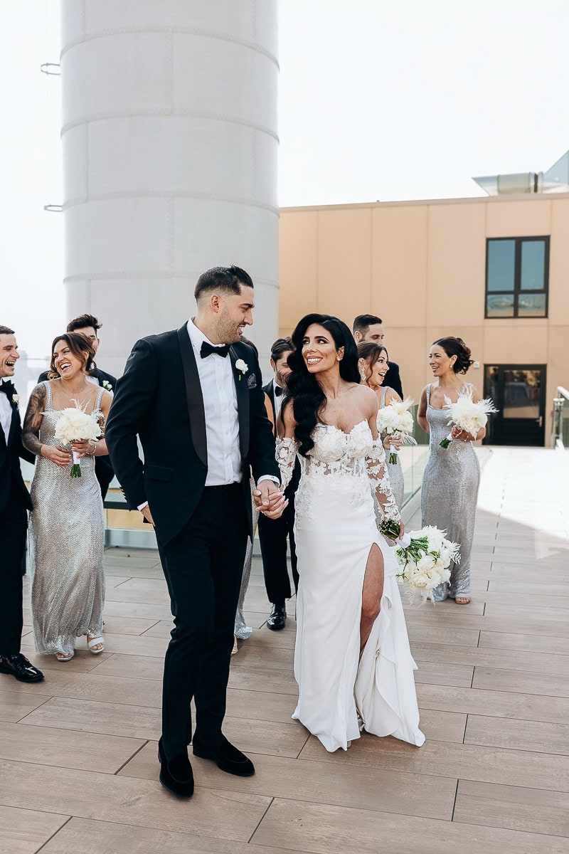 Wedding party walks on a rooftop—bride in lace slit gown, groom in black tux, attendants in silver—at The Switch House by Cescaphe, Philadelphia.