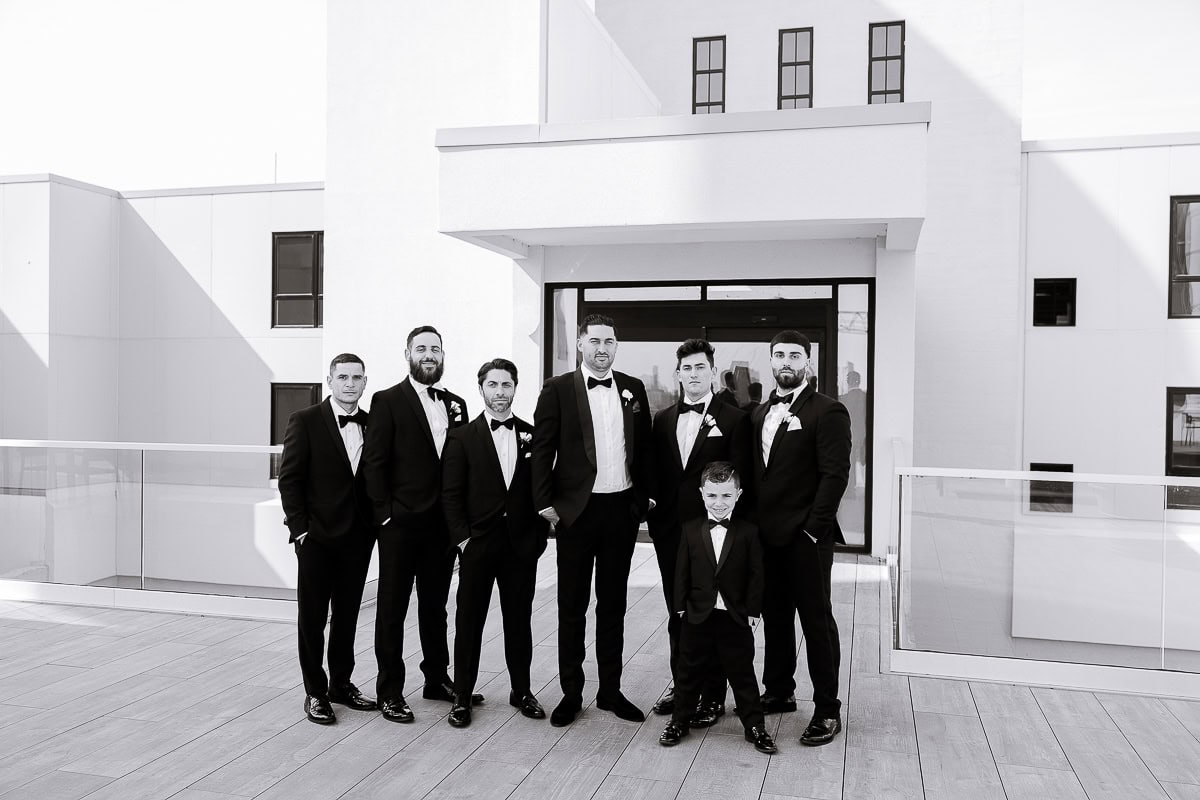 Men in tuxedos with a young attendant on a modern terrace with glass railing at The Switch House by Cescaphe, Philadelphia.