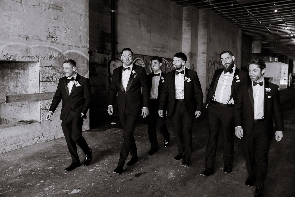 Six men in tuxedos walk through an industrial corridor at The Switch House, Philadelphia.