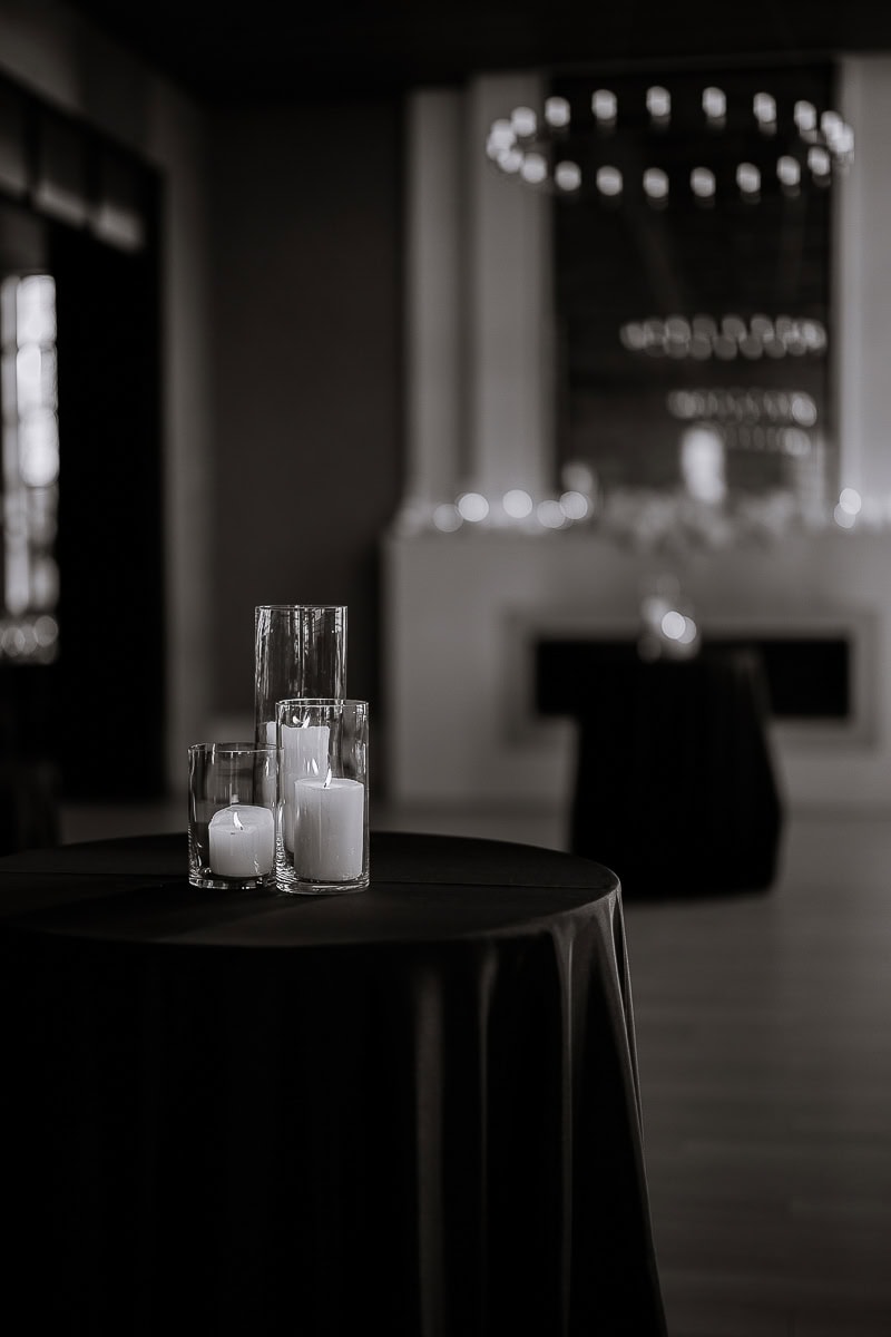 Glass cylinder candles on black-linen cocktail table; blurred chandeliers and fireplace at The Switch House by Cescaphe, Philadelphia.