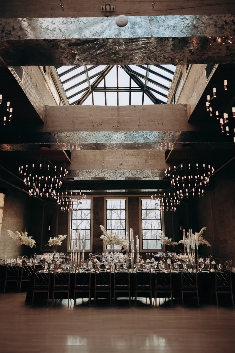 Candlelit banquet under skylight at The Switch House by Cescaphe, Philadelphia; tall crystal tapers, white florals, industrial chandeliers.