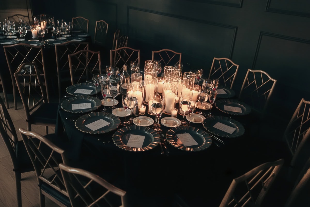 Candlelit round reception table with black linens, gold-rimmed chargers, crystal stemware, and menu cards at The Switch House by Cescaphe, Philadelphia.