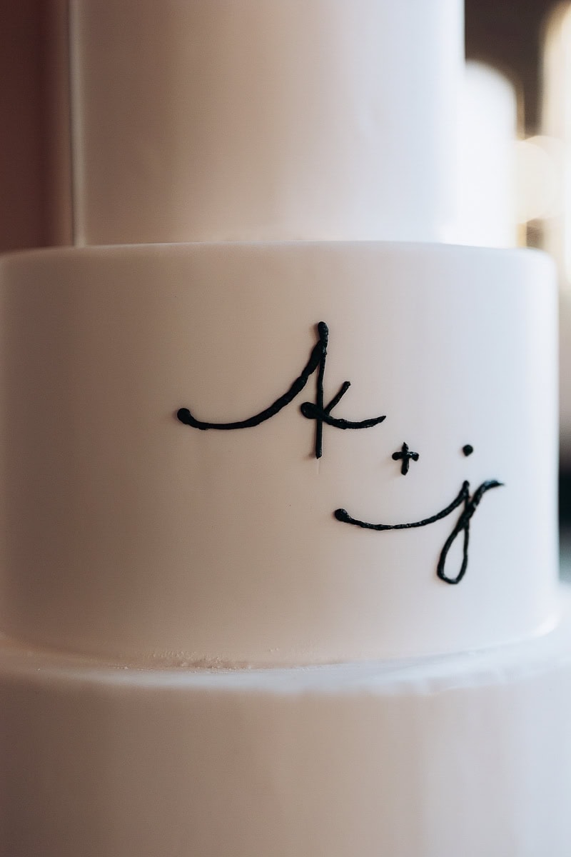 Close-up of white tiered wedding cake with black piped monogram “k + j” at The Switch House by Cescaphe, Philadelphia, PA.