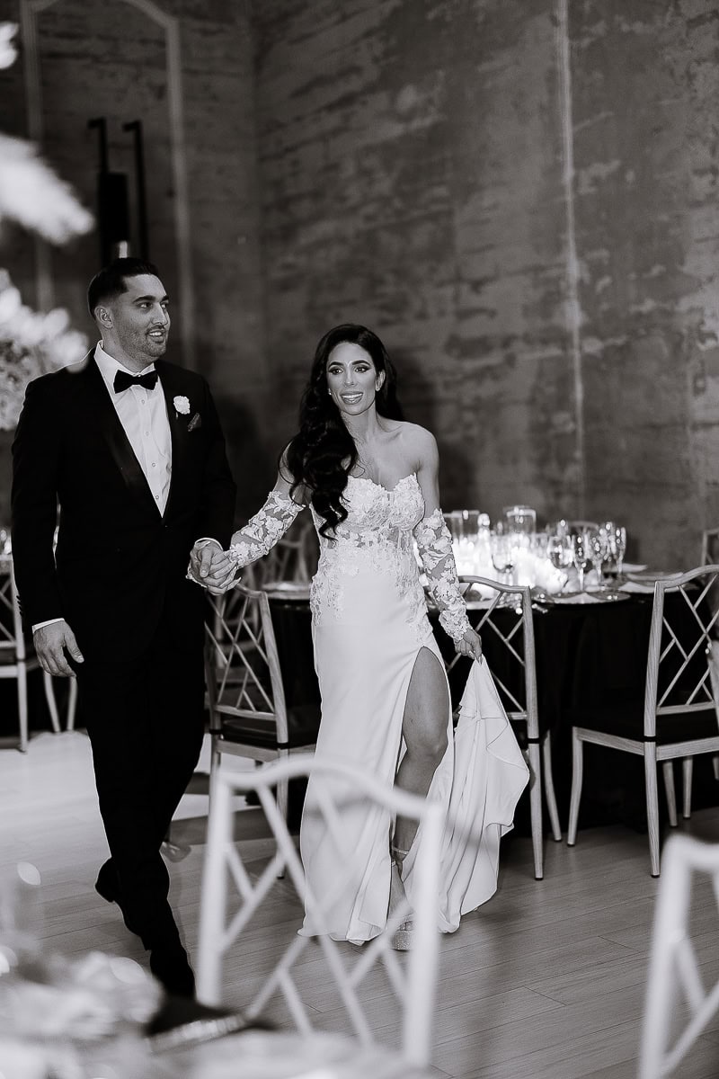 Black-and-white photo of a couple entering a candlelit reception, lace off-shoulder gown with slit and tuxedo, at The Switch House, Philadelphia.