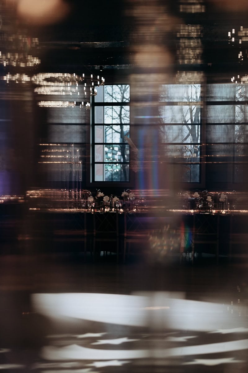 Moody interior with window, chandeliers, and candlelit banquet table; reflections and light streaks over a patterned dance floor at The Switch House, Philadelphia.