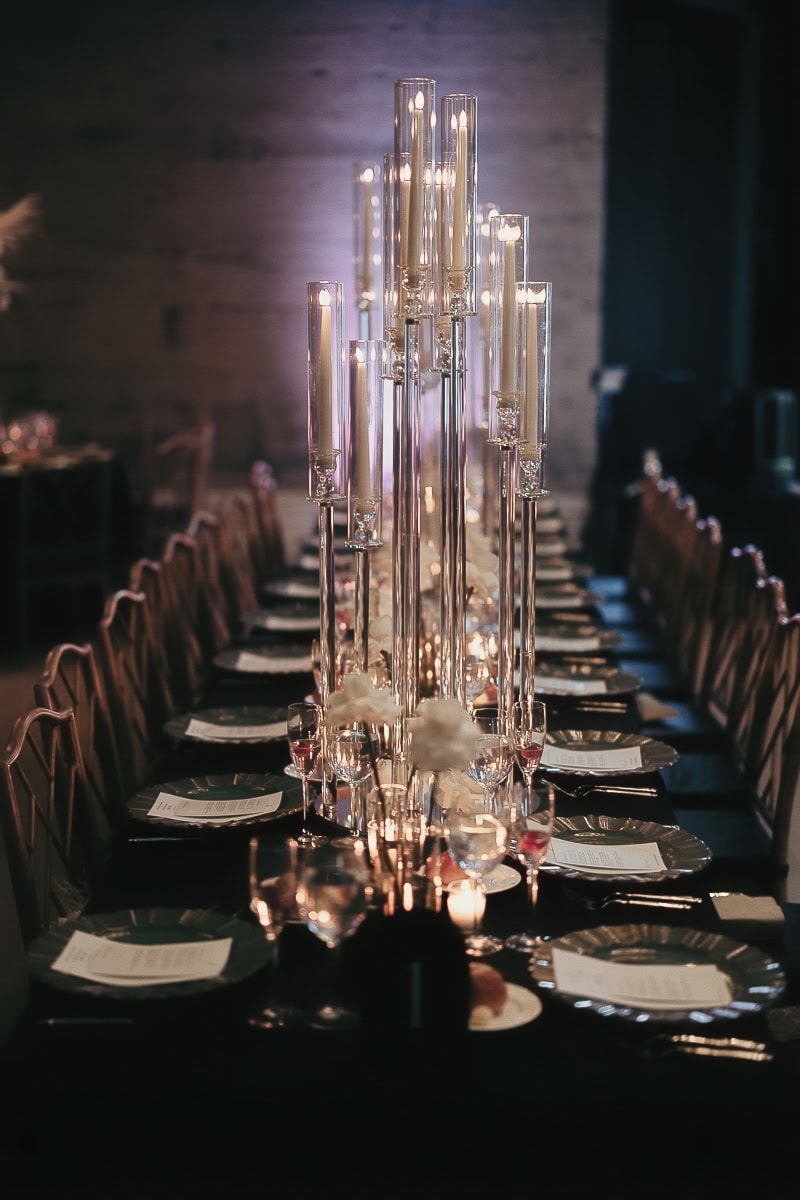 Long black-draped table with tall glass tapers, white roses, menus, and stemware under purple uplighting at The Switch House, Philadelphia.