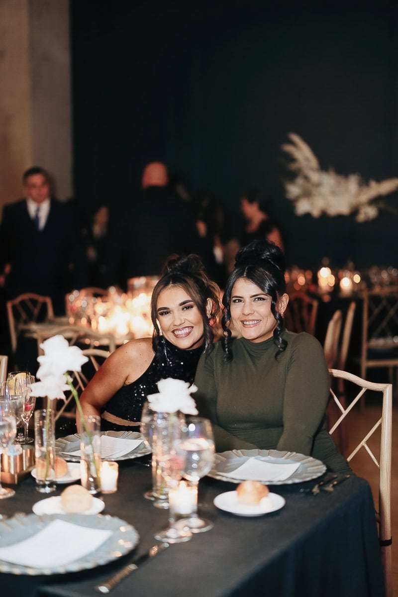 Two wedding guests at a candlelit table with black linen, white florals, and glassware at The Switch House by Cescaphe, Philadelphia.