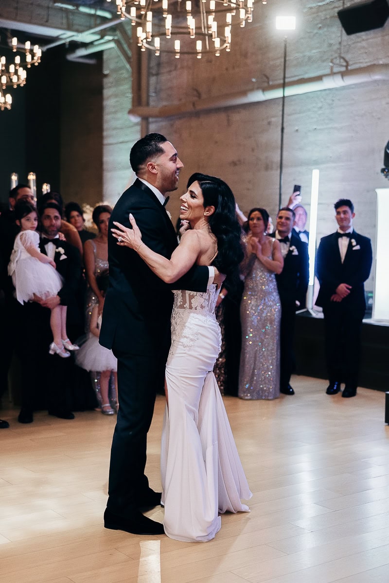 Couple shares first dance on parquet floor under chandeliers, guests in black-tie watching at The Switch House by Cescaphe, Philadelphia.