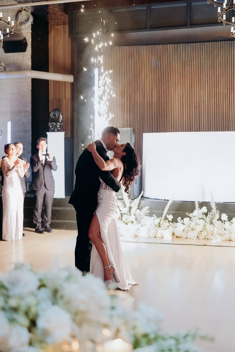 Couple shares first-dance kiss beneath indoor sparkler fountain, white florals and LED backdrop at The Switch House by Cescaphe, Philadelphia.