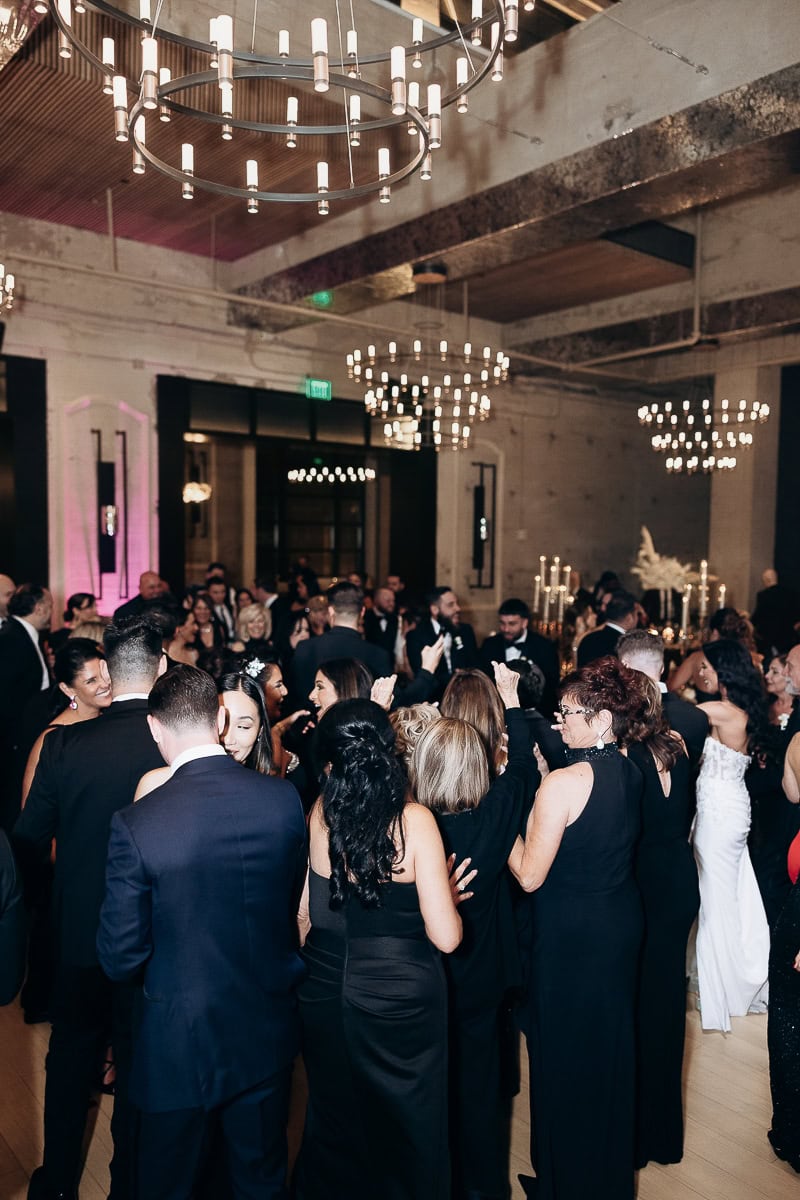 Black-tie guests dance under modern chandeliers in an industrial-chic ballroom with candelabras at The Switch House by Cescaphe, Philadelphia, PA.