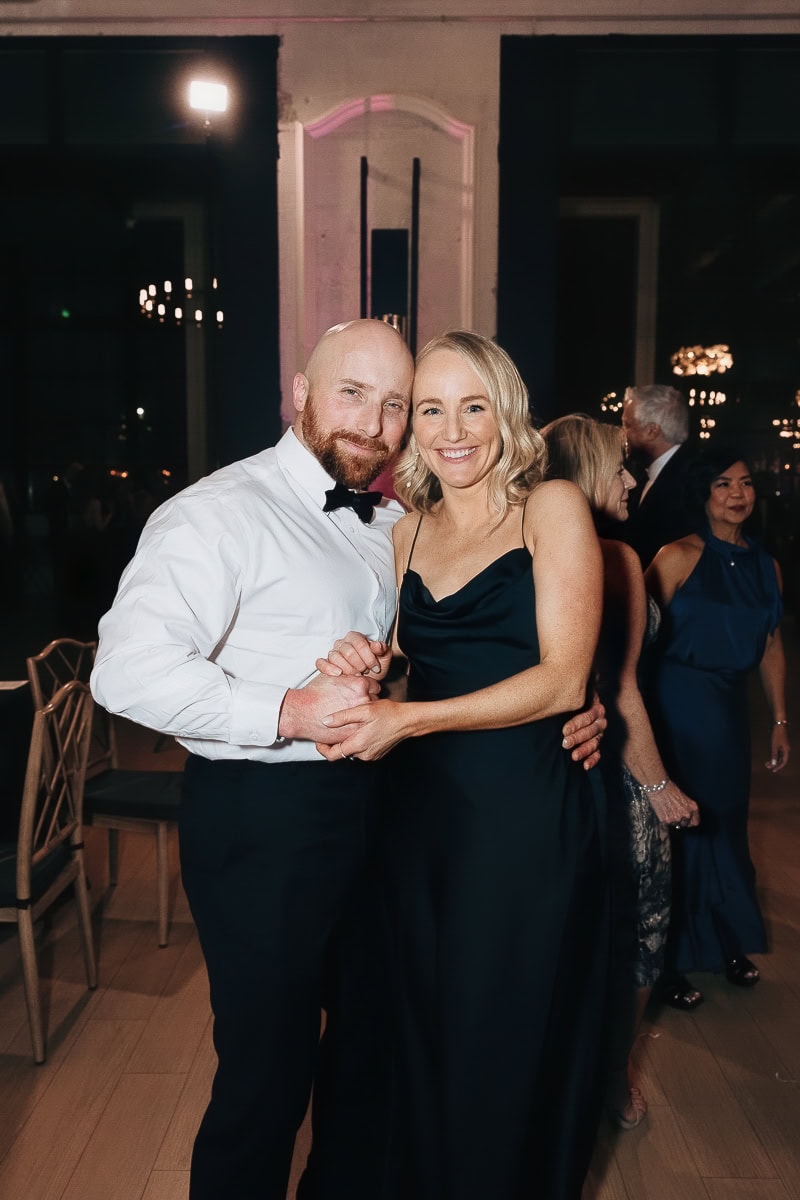 Two guests—one in a tuxedo, one in a black satin gown—dancing under chandeliers at The Switch House by Cescaphe, Philadelphia.