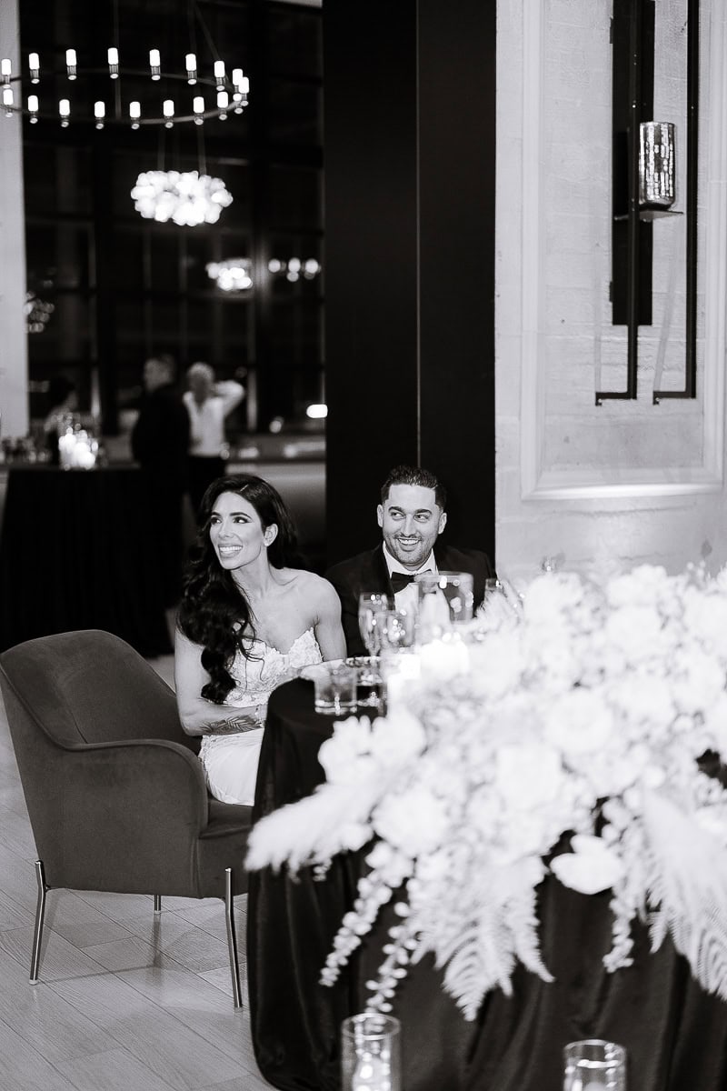 Two newlyweds seated at a candlelit sweetheart table with lush white florals during a black-tie reception at The Switch House, Philadelphia.