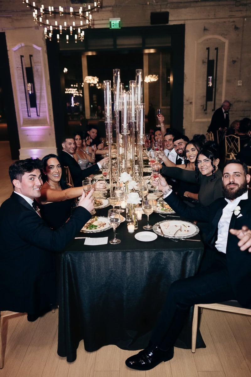 Guests in formal attire raise glasses along a candlelit banquet table with black linens at The Switch House by Cescaphe, Philadelphia.