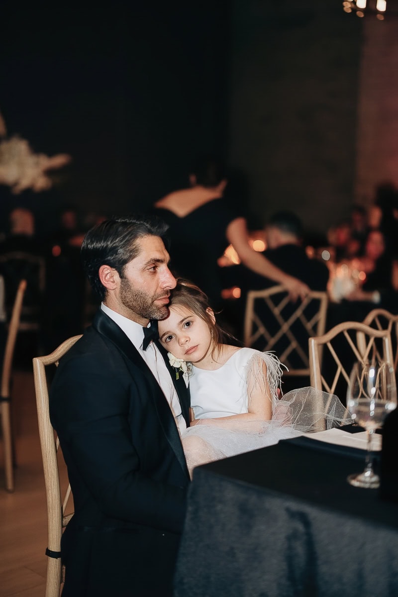 Man in a tuxedo holds a young girl in a white dress during a candlelit wedding reception at The Switch House by Cescaphe, Philadelphia, PA.