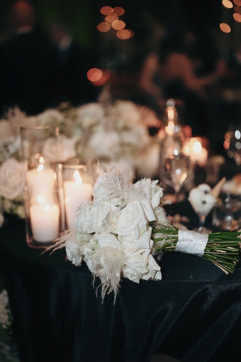 White rose bouquet with pearl wrap on black satin beside glass pillar candles; reception detail at The Switch House by Cescaphe, Philadelphia, PA.