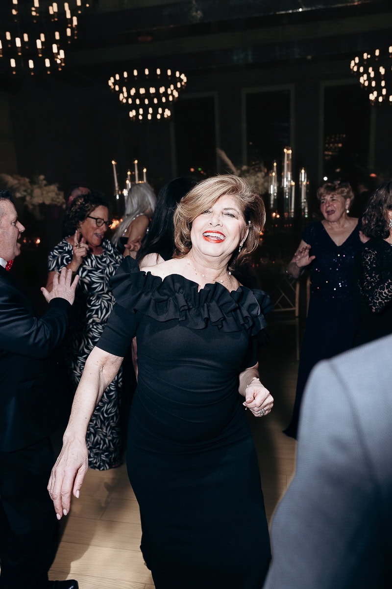 Guest in black off-shoulder ruffled dress dancing under chandeliers amid candlelit guests at The Switch House by Cescaphe, Philadelphia, PA.