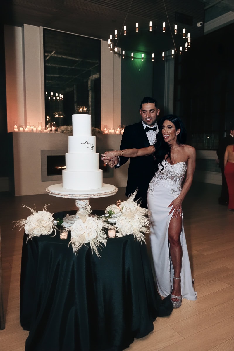 Couple cutting a four-tier white cake on black-draped table with white roses and candles at The Switch House by Cescaphe, Philadelphia.