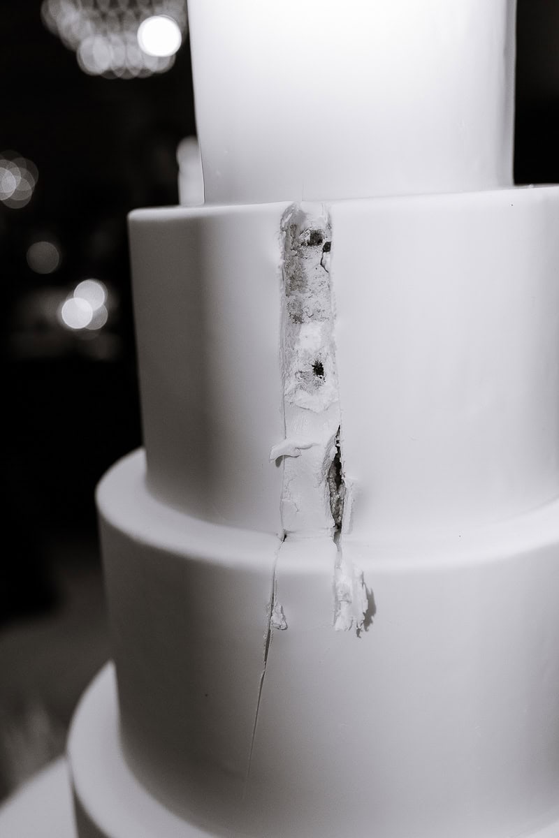 Black-and-white close-up of a tiered wedding cake with a vertical crack in the fondant.