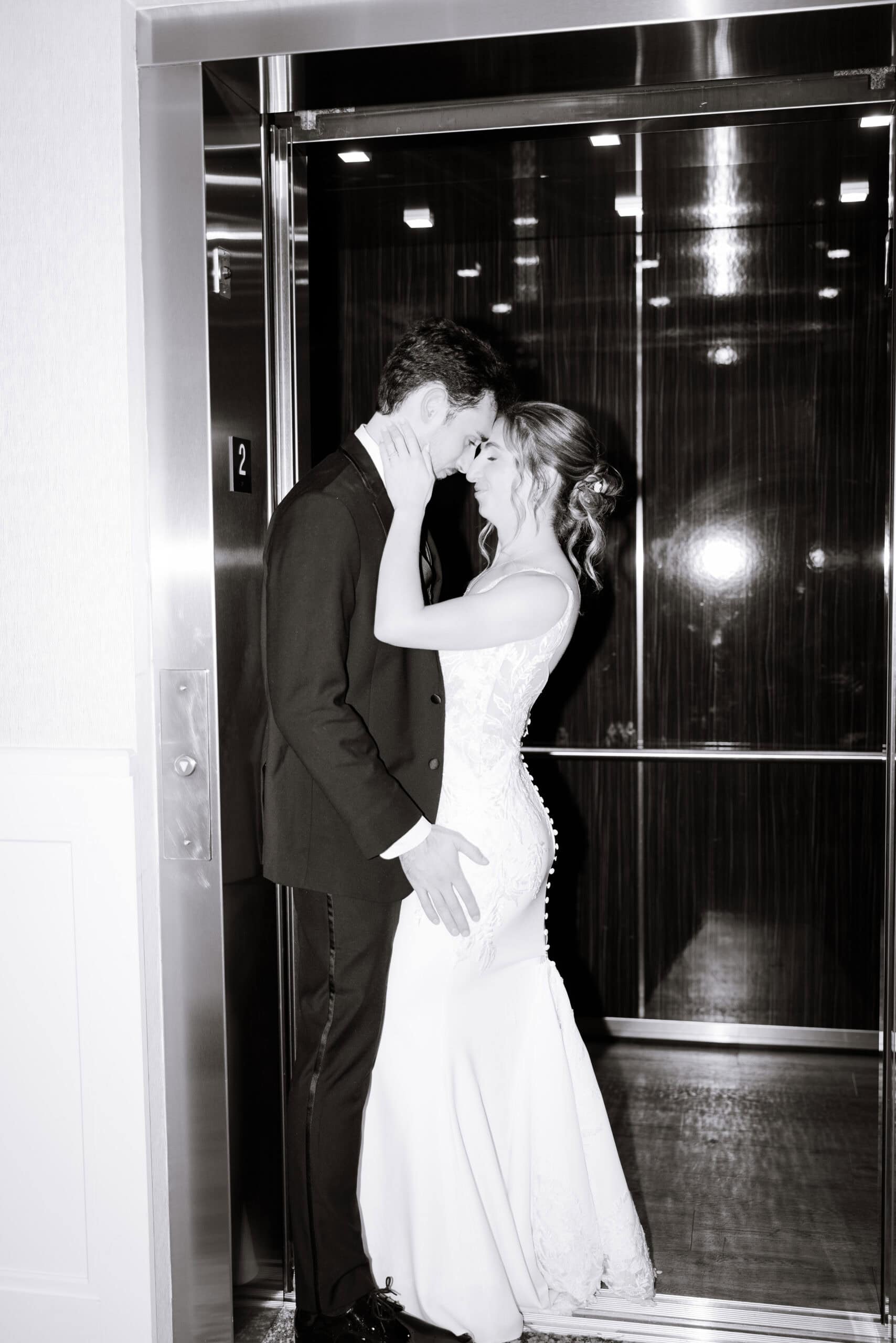 Bride and groom embracing closely inside a modern elevator with reflective metallic walls at Tyde at Walnut Beach, Milford, CT.