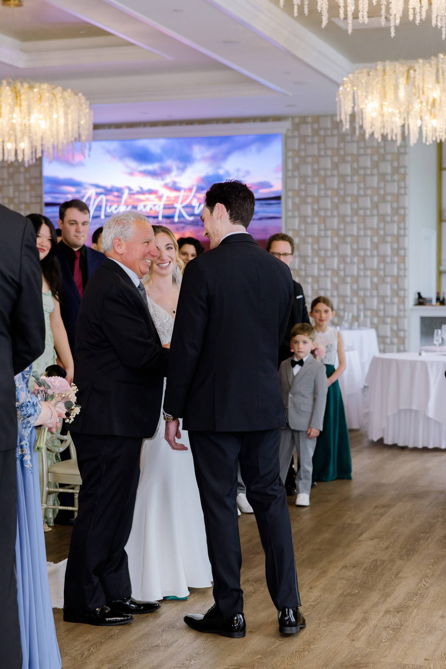 Groom and elder smiling during wedding ceremony with bride and guests in the background at Tyde at Walnut Beach, Milford, CT.