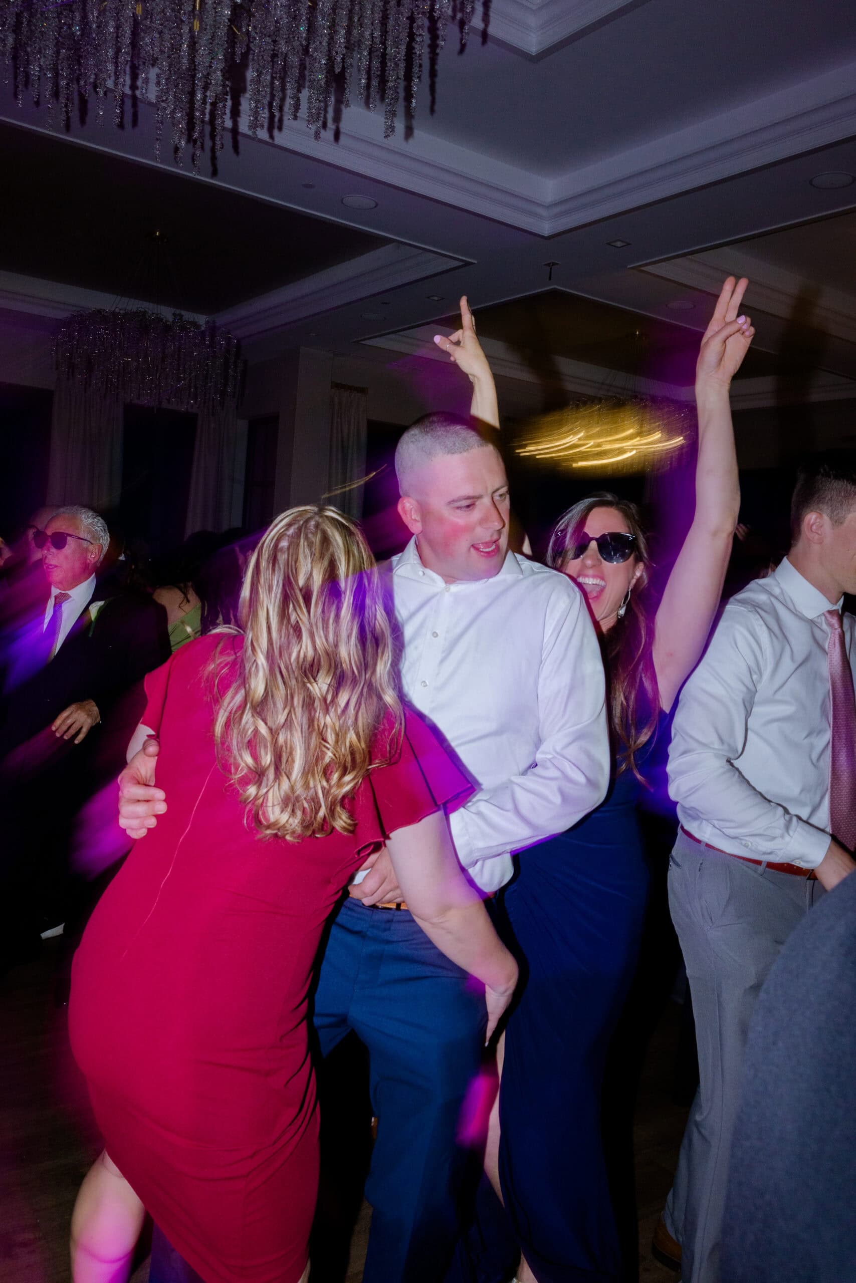 People dancing energetically indoors under crystal chandeliers with purple and golden lighting effects at Tyde at Walnut Beach, Milford, CT.