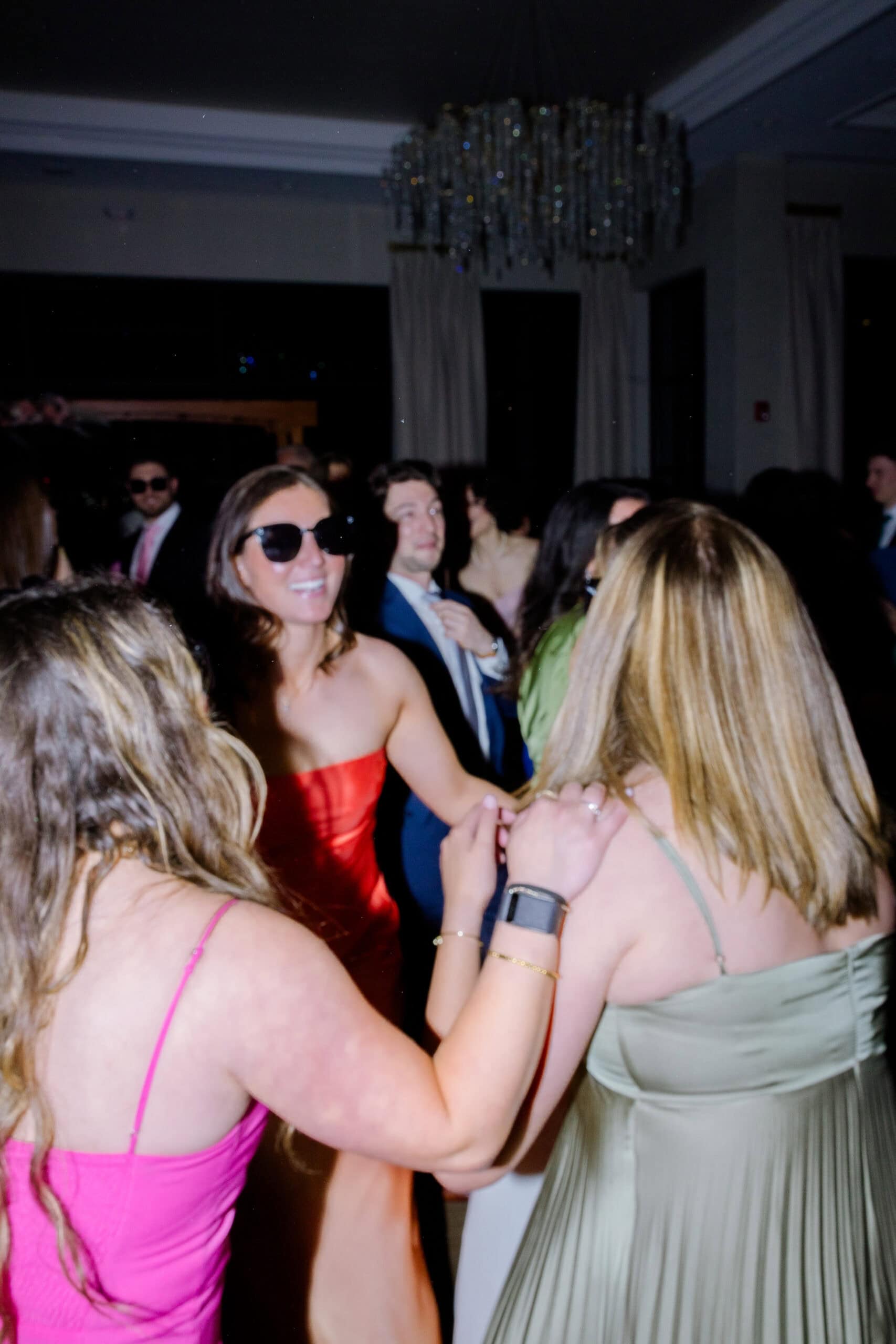 Guests dancing closely in elegant attire under a crystal chandelier at a wedding reception in Tyde at Walnut Beach, Milford, CT.