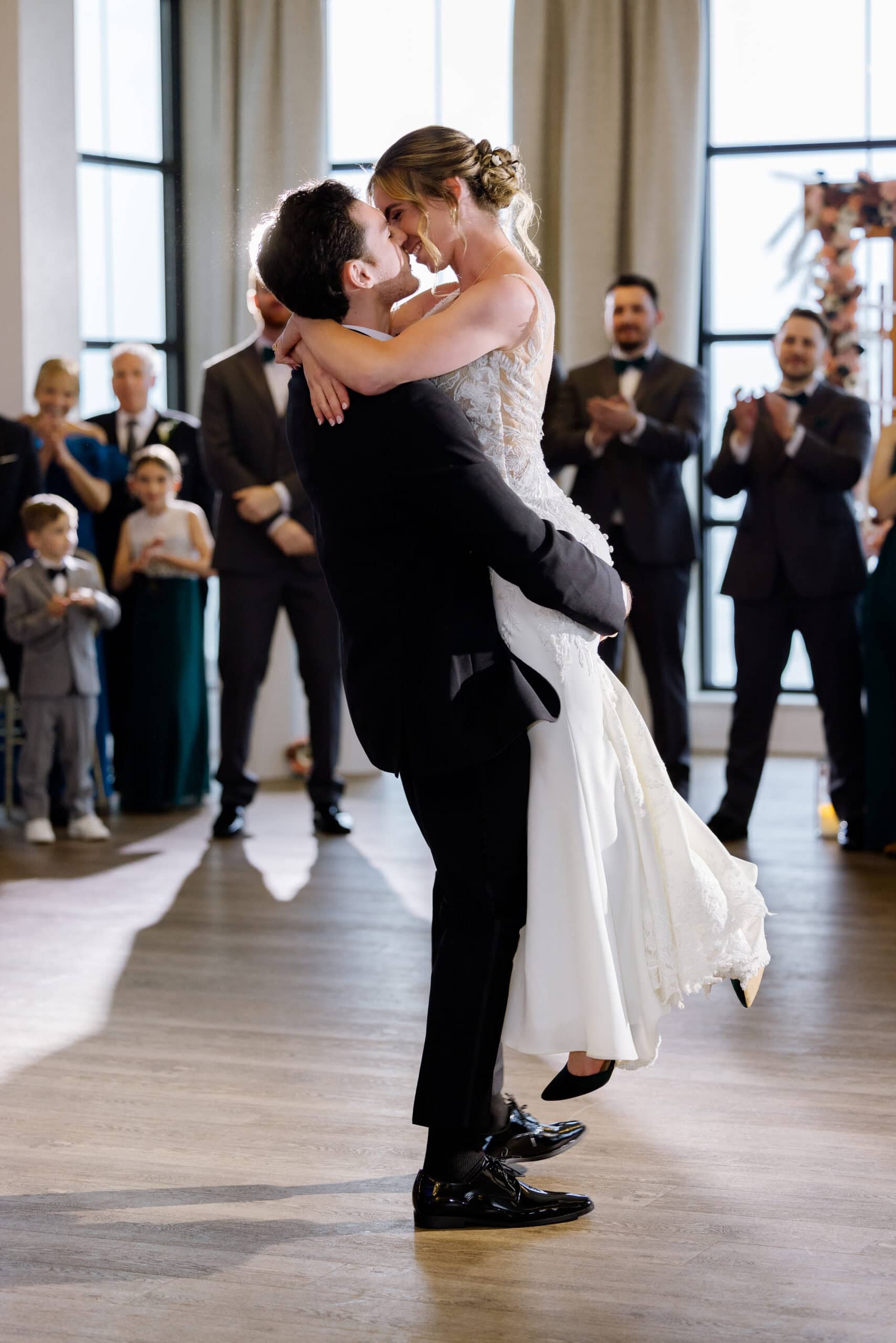 Bride and groom sharing an intimate dance embrace while guests applaud in a sunlit venue at Tyde at Walnut Beach, Milford, CT.