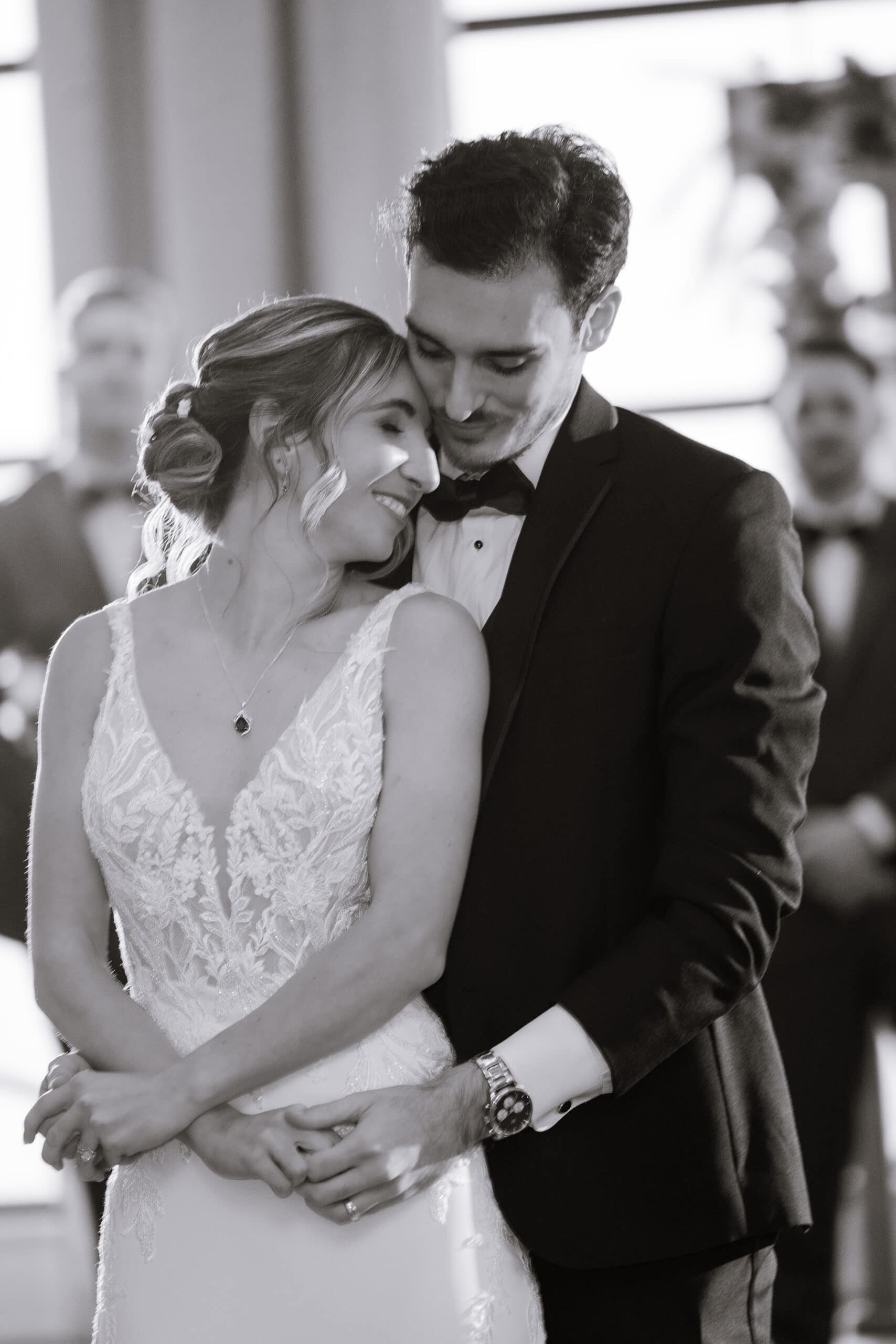 Black and white close-up of a bride and groom in an intimate embrace, bride in lace wedding dress, groom in tuxedo, soft natural light
