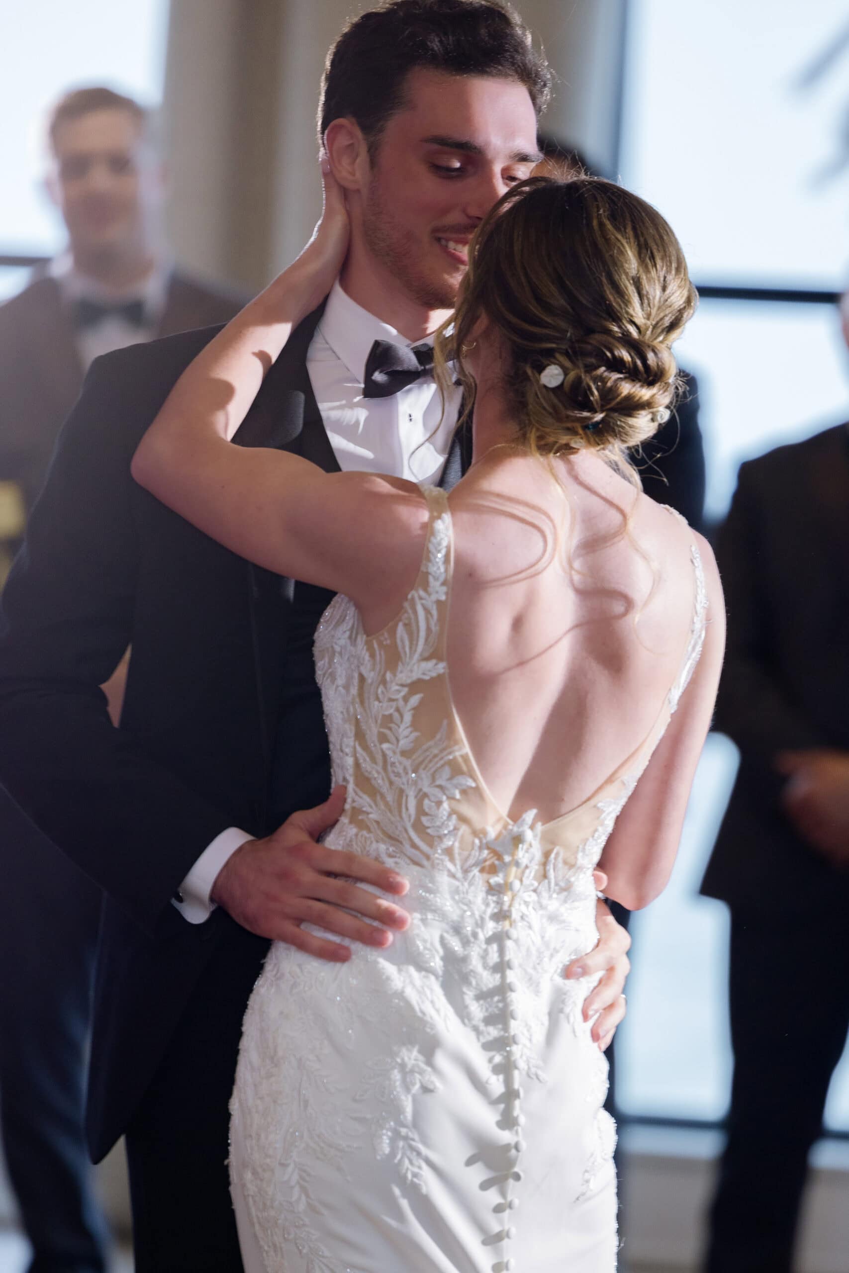 Close-up of a bride and groom sharing an intimate first dance, highlighting the bride's lace wedding dress back and groom's black tuxedo.