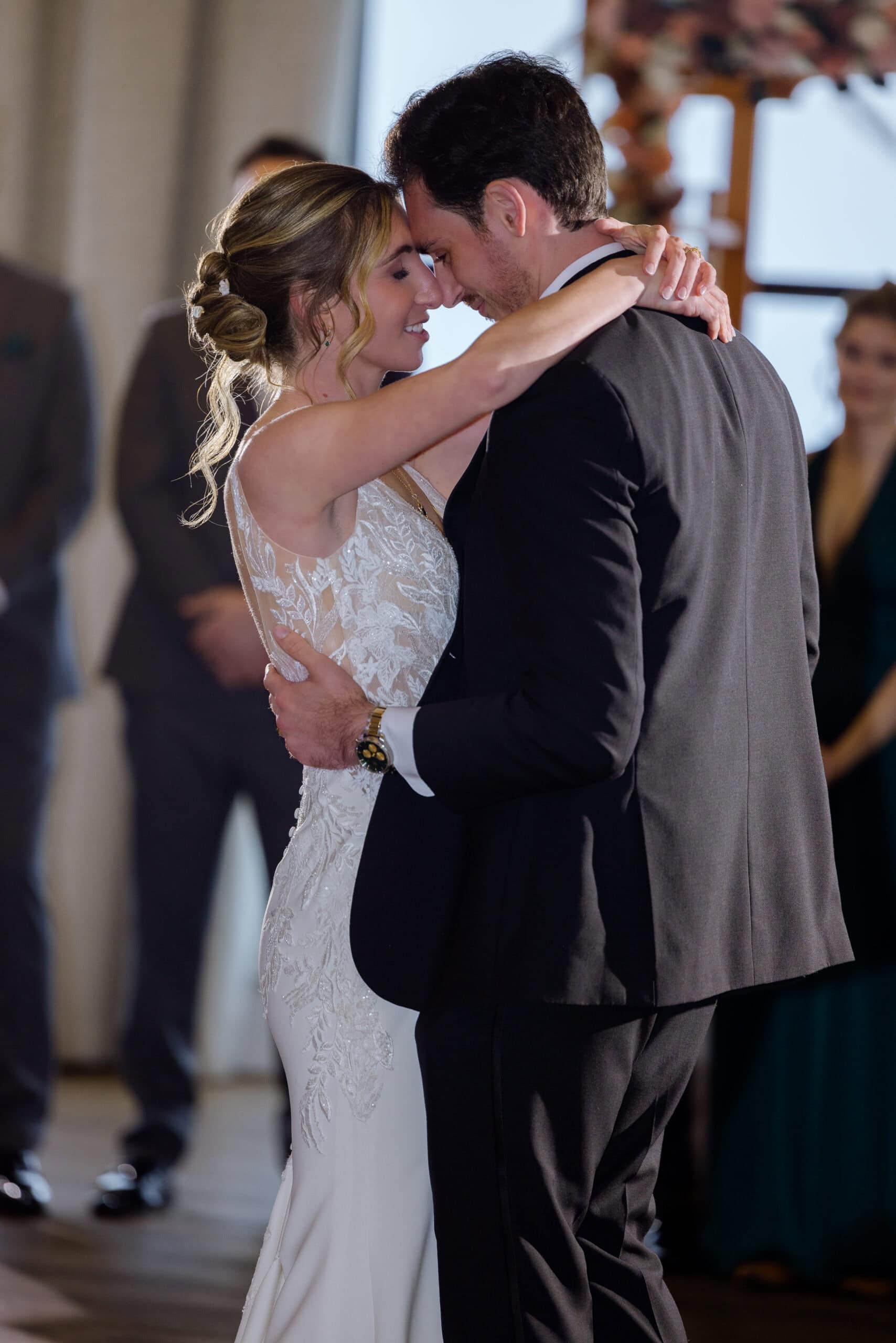 Bride and groom in an intimate embrace with foreheads touching during their wedding first dance, showcasing lace wedding dress and black suit.