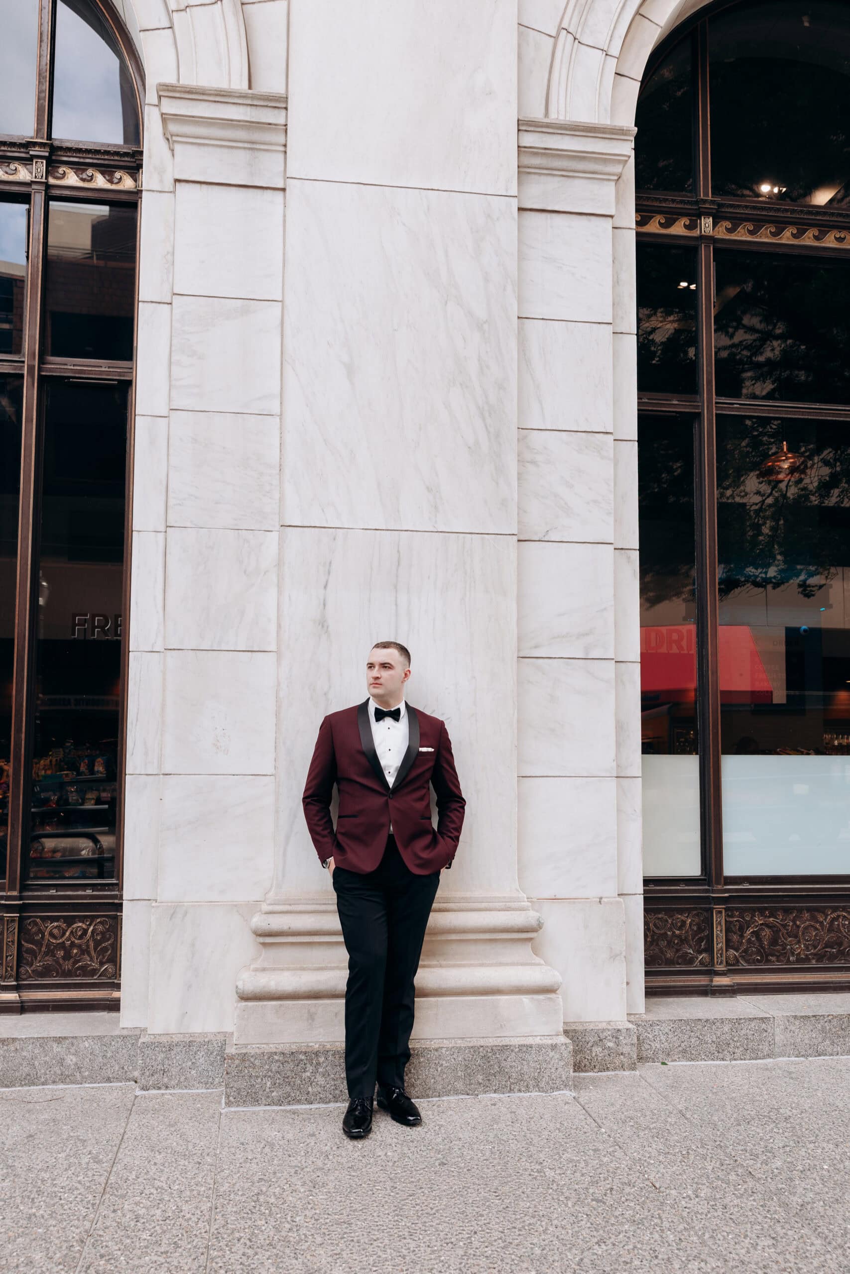 Man in burgundy tuxedo with black lapels standing against a large white marble column at Union Trust, Philadelphia.