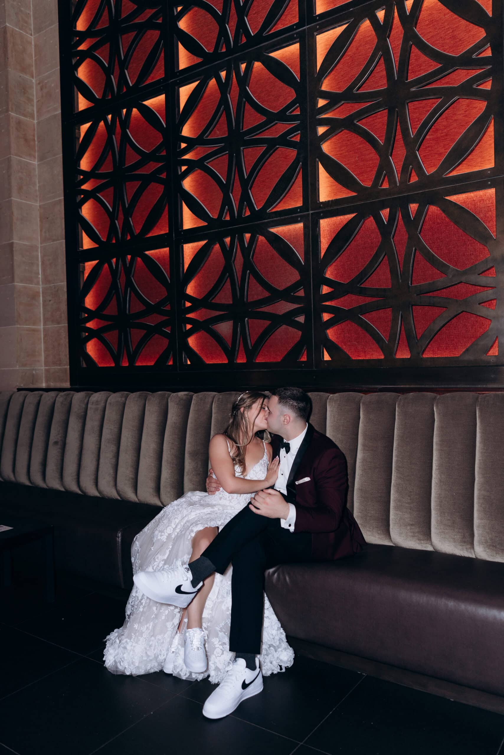 Newlywed couple kissing on a velvet banquette under a black geometric lattice with amber lighting at Union Trust, Philadelphia.