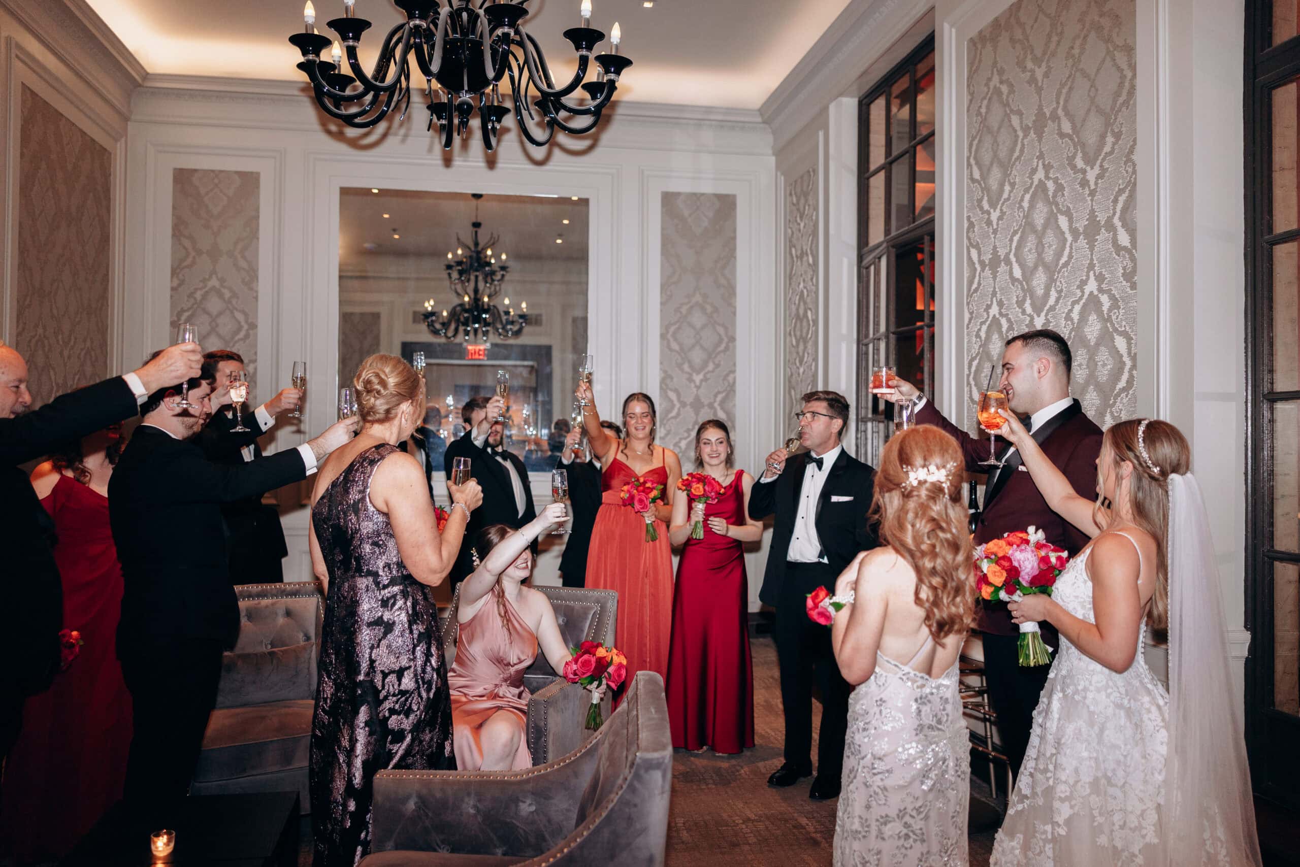 Wedding guests in formalwear raising champagne glasses in a toast inside a richly decorated room at Union Trust, Philadelphia.