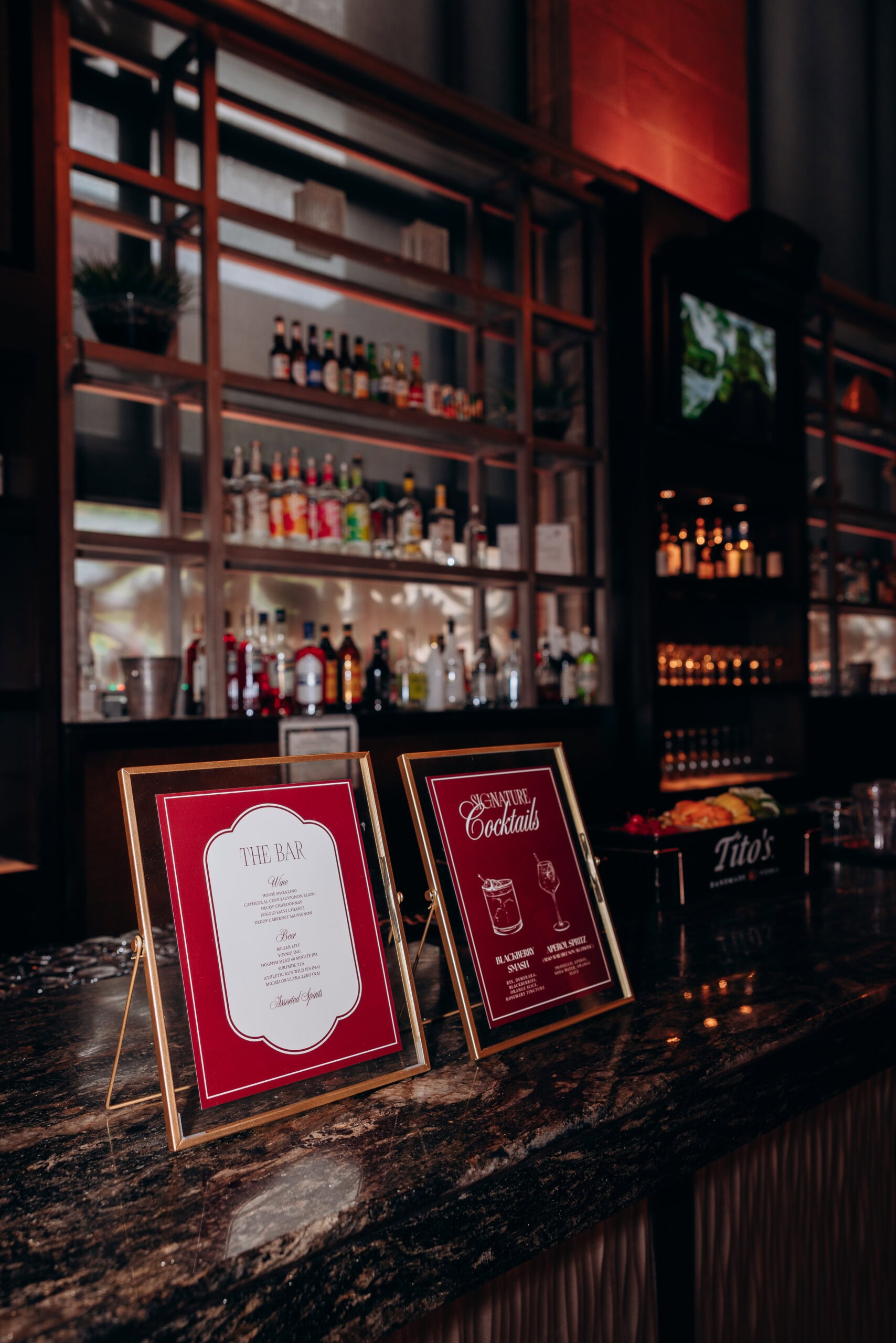 Framed bar and cocktail menus on marble counter with illuminated shelves of assorted liquor bottles in the background at Union Trust, Philadelphia.