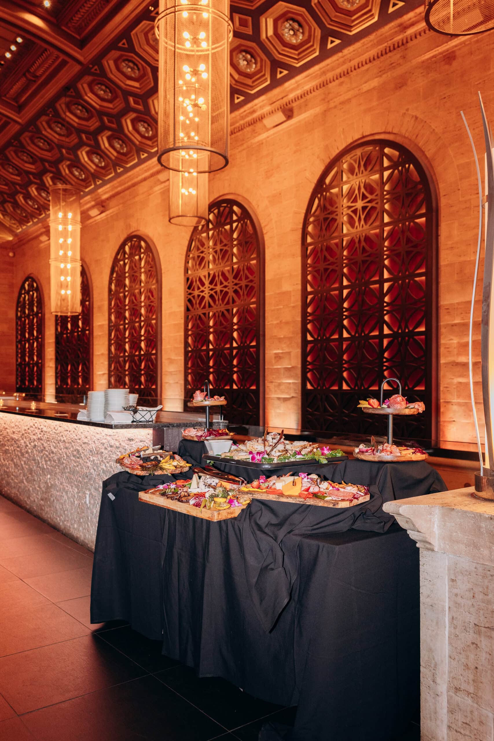 Gourmet food display on black-draped tables beneath ornate wood-paneled ceiling and patterned arched windows at Union Trust, Philadelphia, PA.