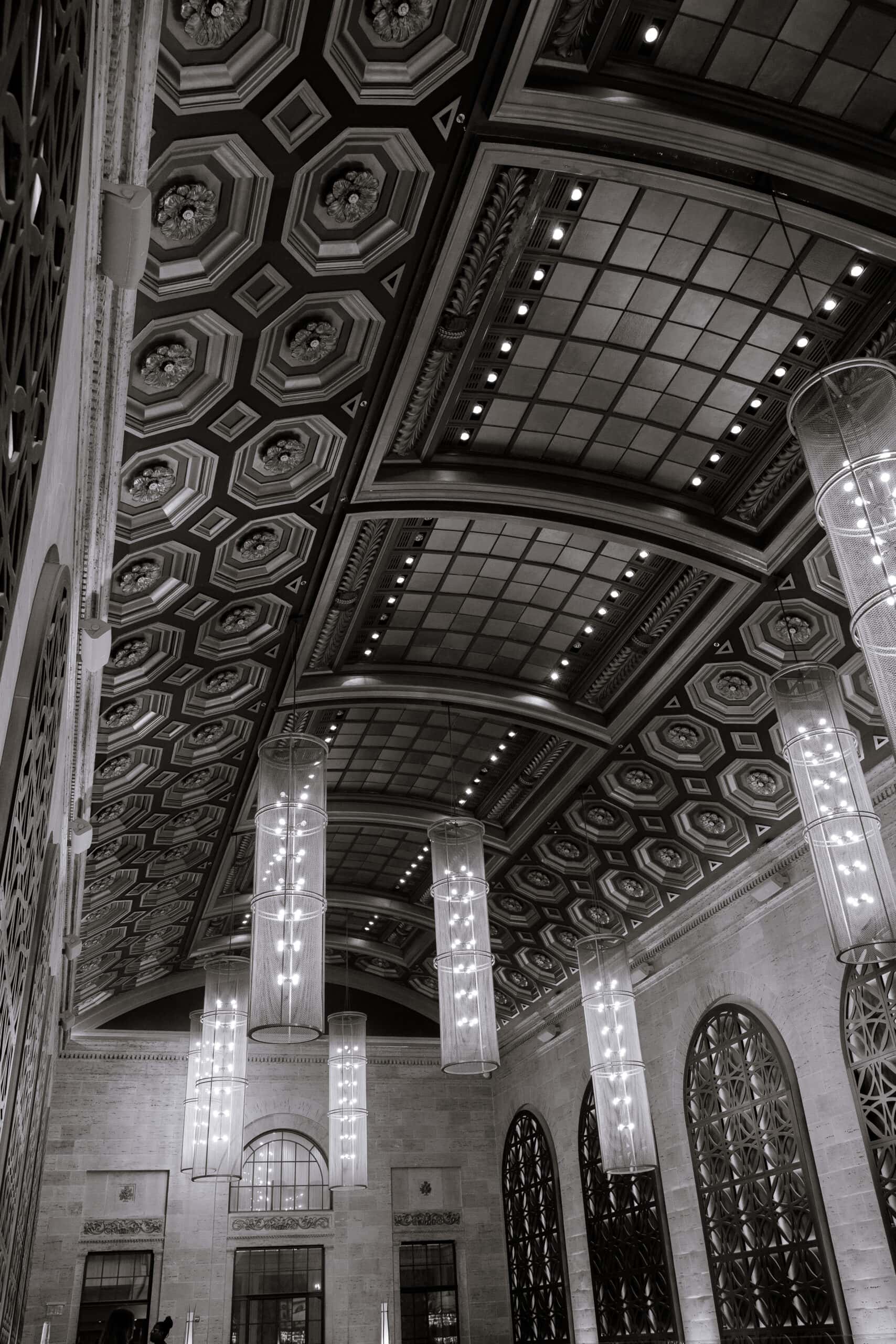 Black and white photo of Union Trust's ornate coffered ceiling with floral plaster details and hanging cylindrical pendant lights in Philadelphia.