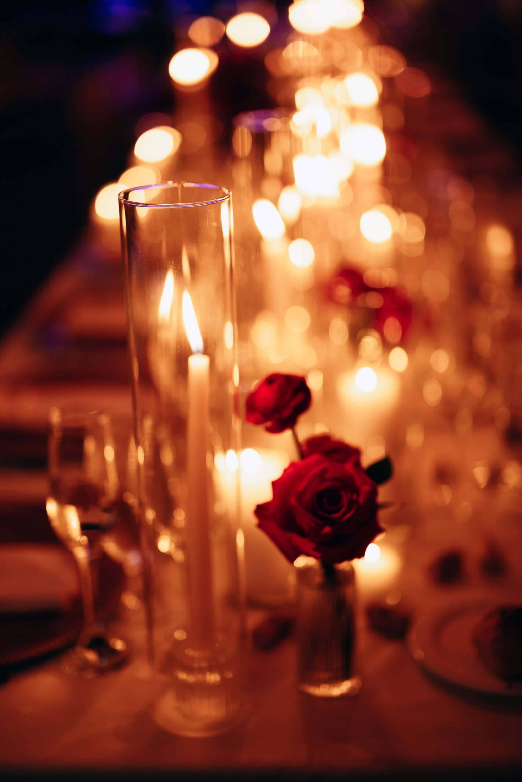 Tall glass candle holders with lit candles and red roses on a softly illuminated table at Union Trust, Philadelphia.