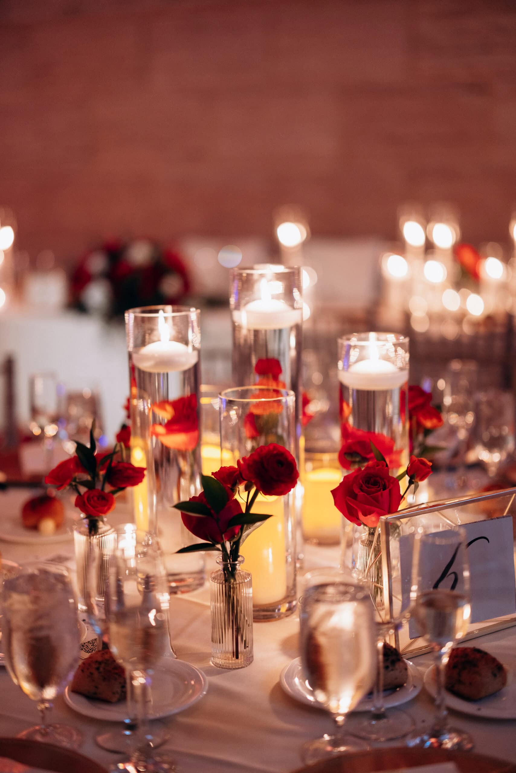 Close-up of a wedding table at Union Trust, Philadelphia, with floating candles in glass cylinders and red roses in small vases, softly lit.