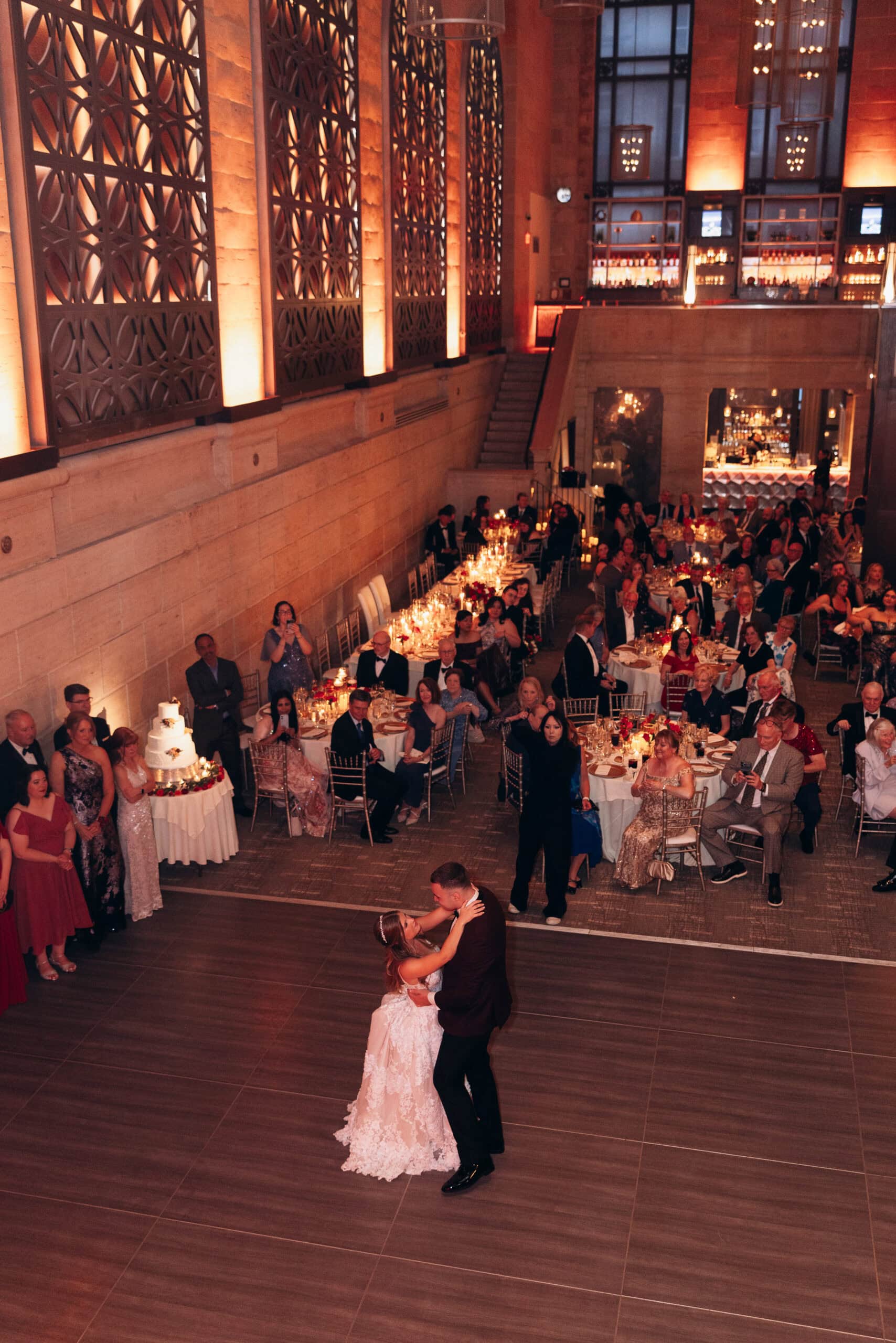 Bride and groom dancing closely on a spacious wooden floor at Union Trust, Philadelphia, surrounded by seated guests and illuminated by warm ambient lighting.