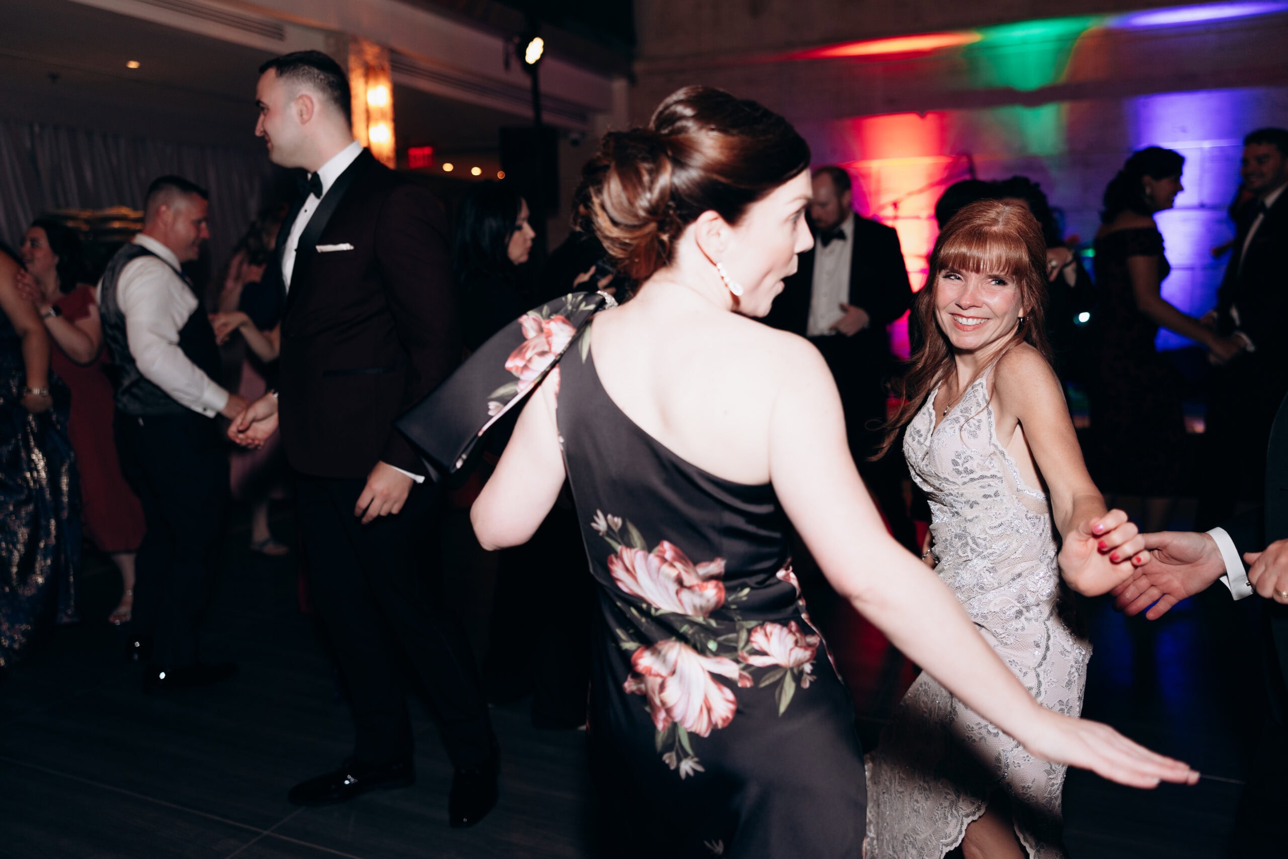 Guests in formal dresses and tuxedos dancing at a wedding reception with colorful uplighting at Union Trust, Philadelphia, PA.