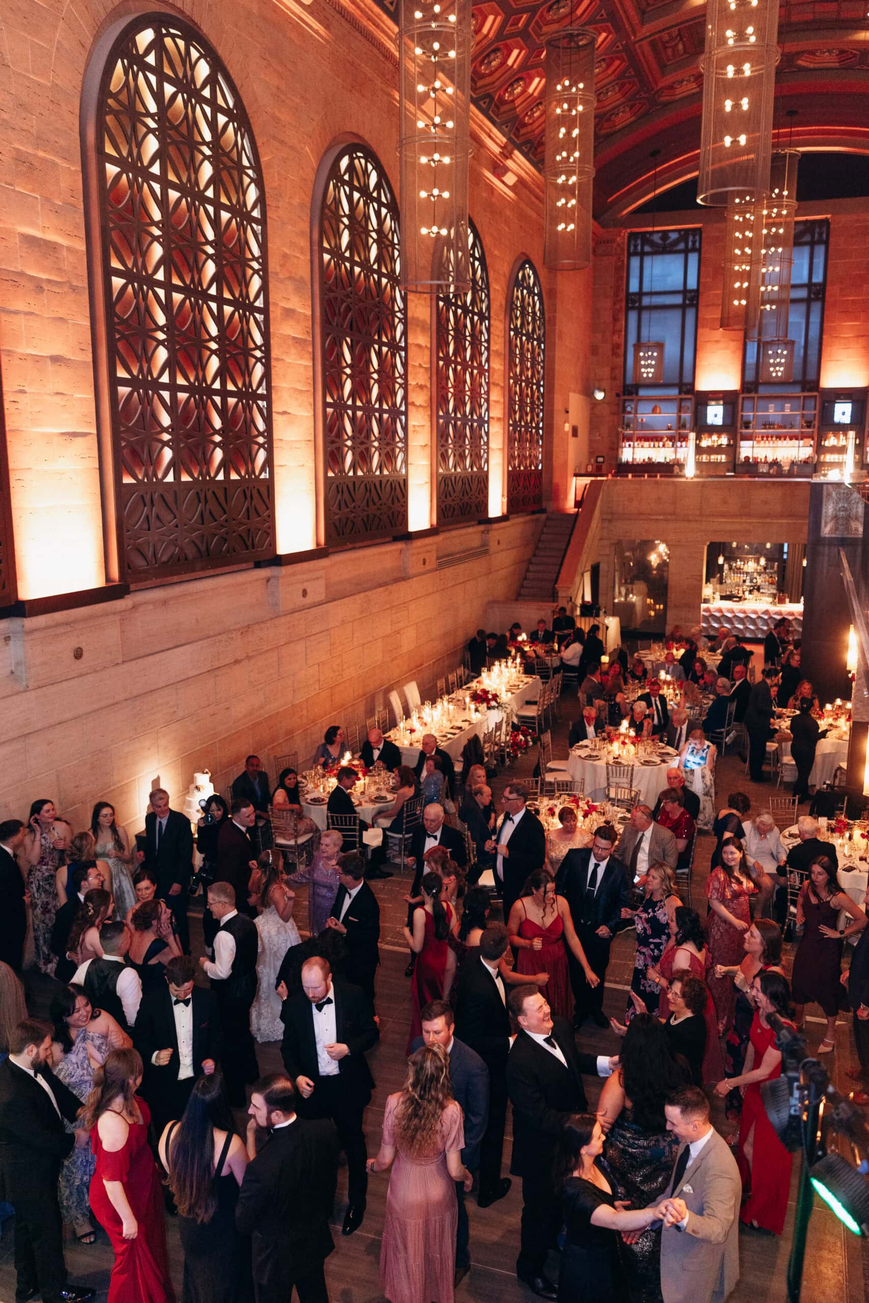 Guests in formal wear dance and mingle in a grand hall with arched decorative windows and warm lighting at Union Trust, Philadelphia.