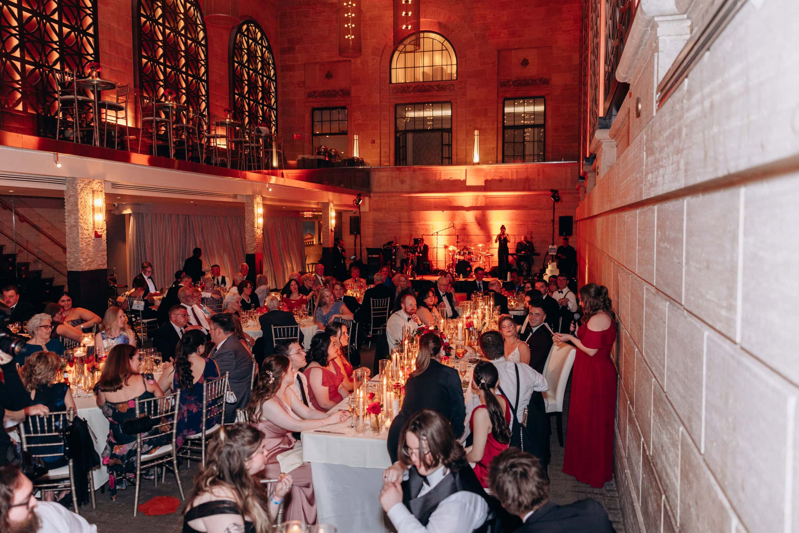 Wedding reception with guests seated at candlelit tables in a grand hall with arched windows and warm amber lighting at Union Trust, Philadelphia.