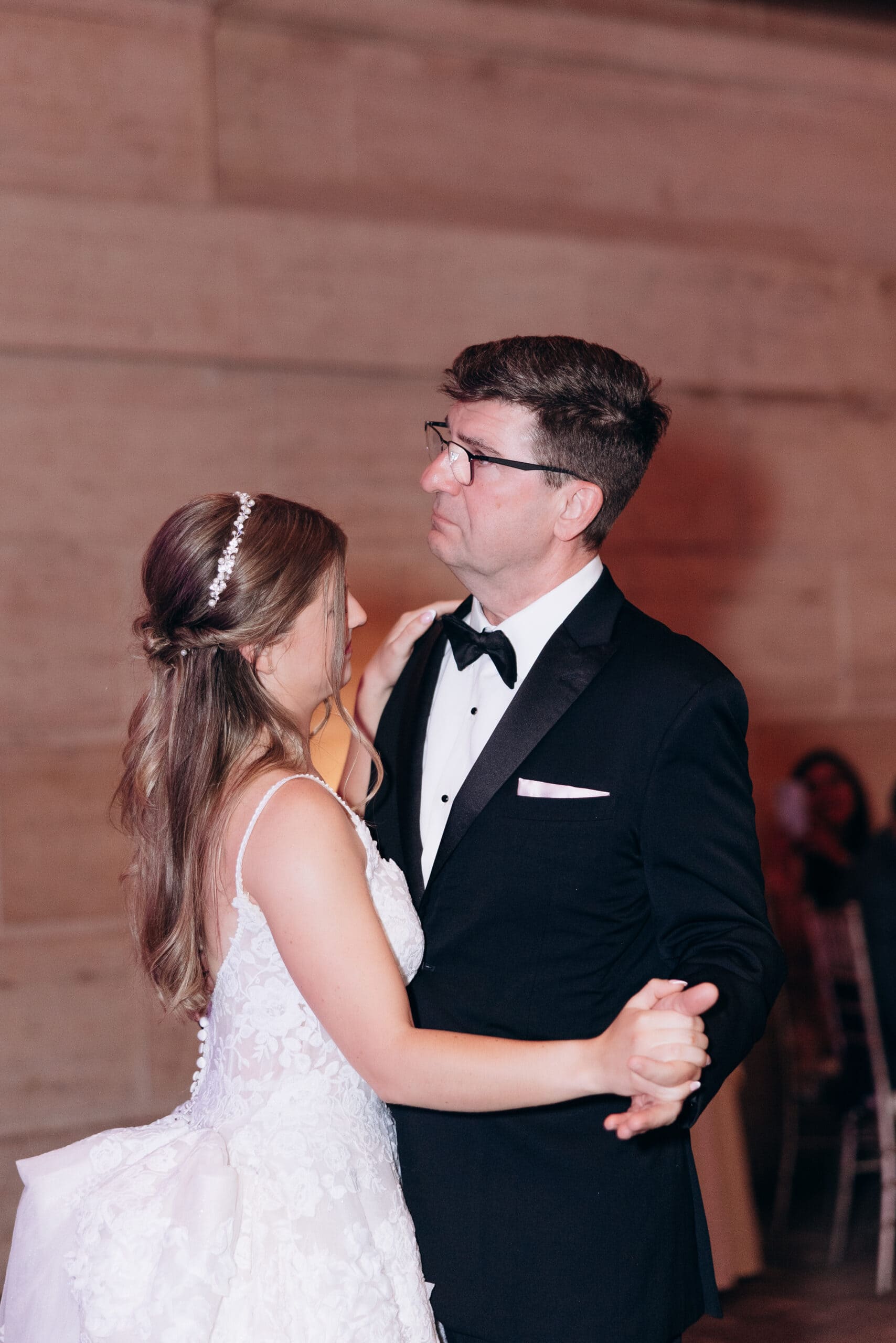 Bride in lace wedding dress dancing with her father in a black tuxedo, against a stone wall at Union Trust, Philadelphia.
