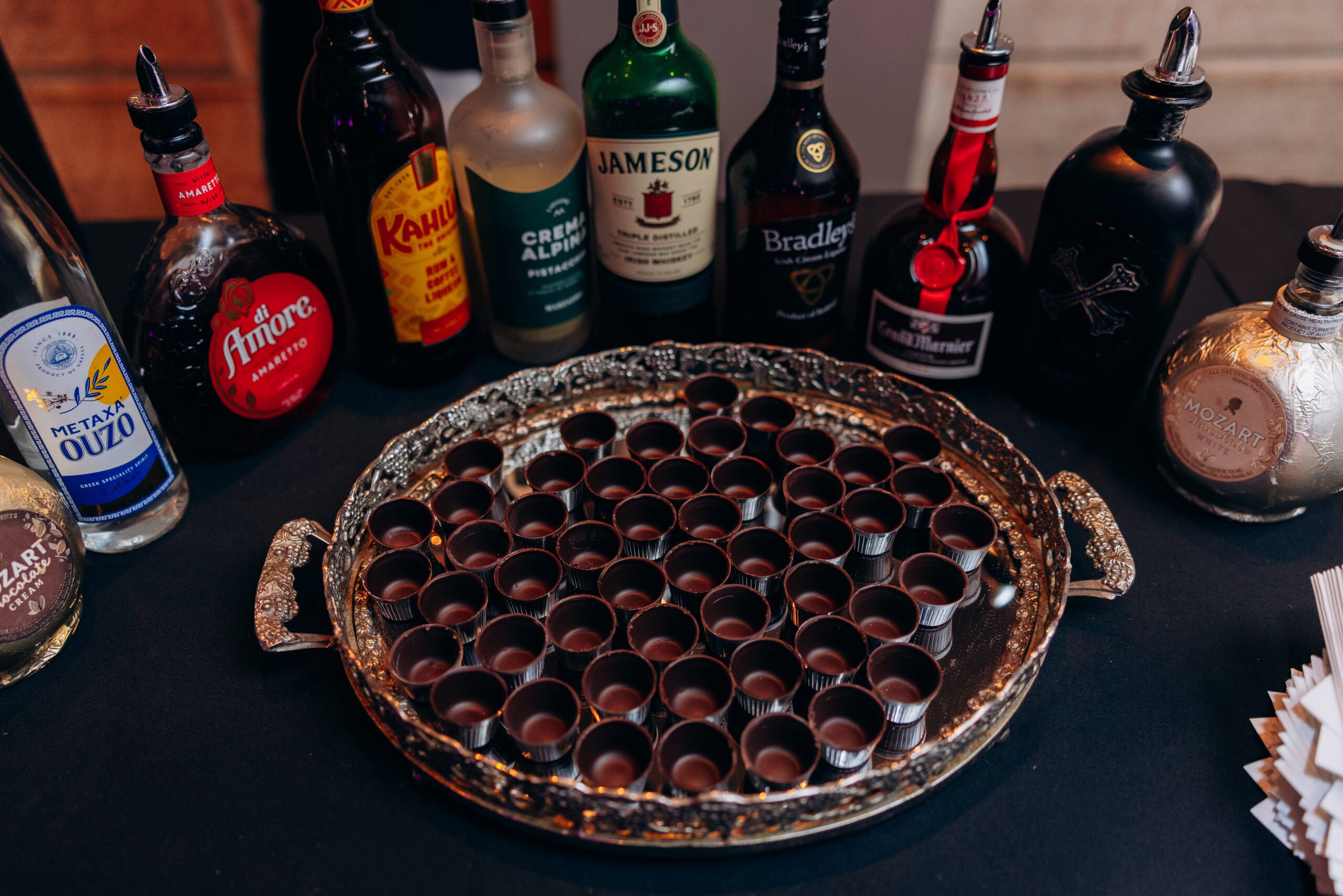 Silver tray with chocolate shot glasses in front of assorted liqueur bottles on black tablecloth at Union Trust, Philadelphia.