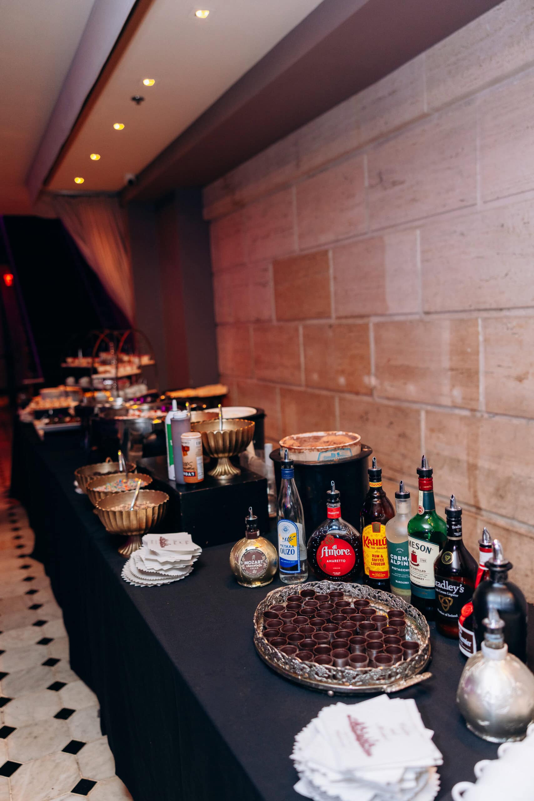 Long table with assorted liqueur bottles, gold serving bowls, chocolate cups, and napkins arranged for a sophisticated event at Union Trust, Philadelphia.