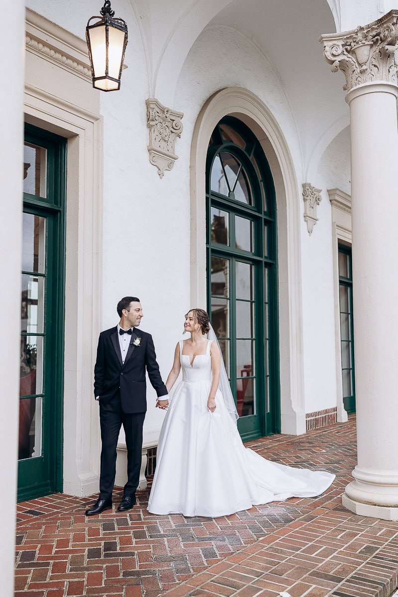 Bride and groom holding hands under white arches with green windows and brick floor at Westchester Country Club, Rye, NY.