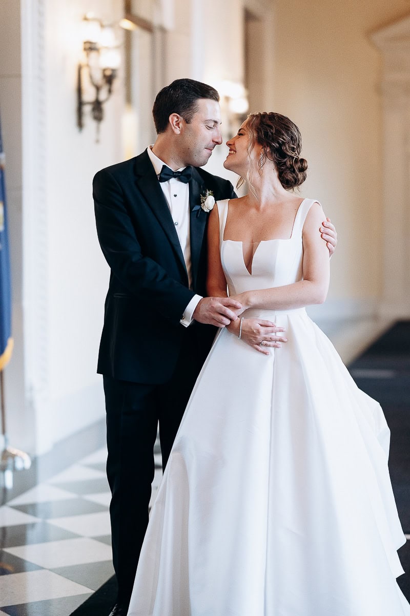 Groom in black tuxedo and bride in white wedding dress sharing an intimate moment inside Westchester Country Club, Rye, NY.
